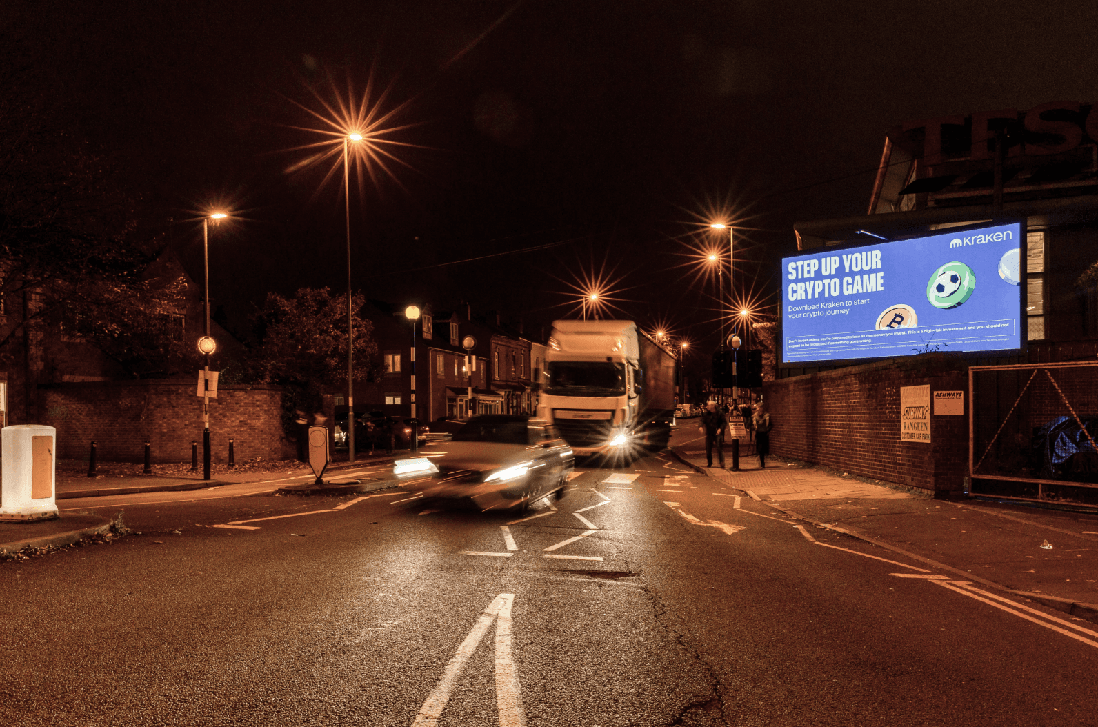Kraken ‘Step Up Your Crypto Game’ billboard on a night street by a Tesco