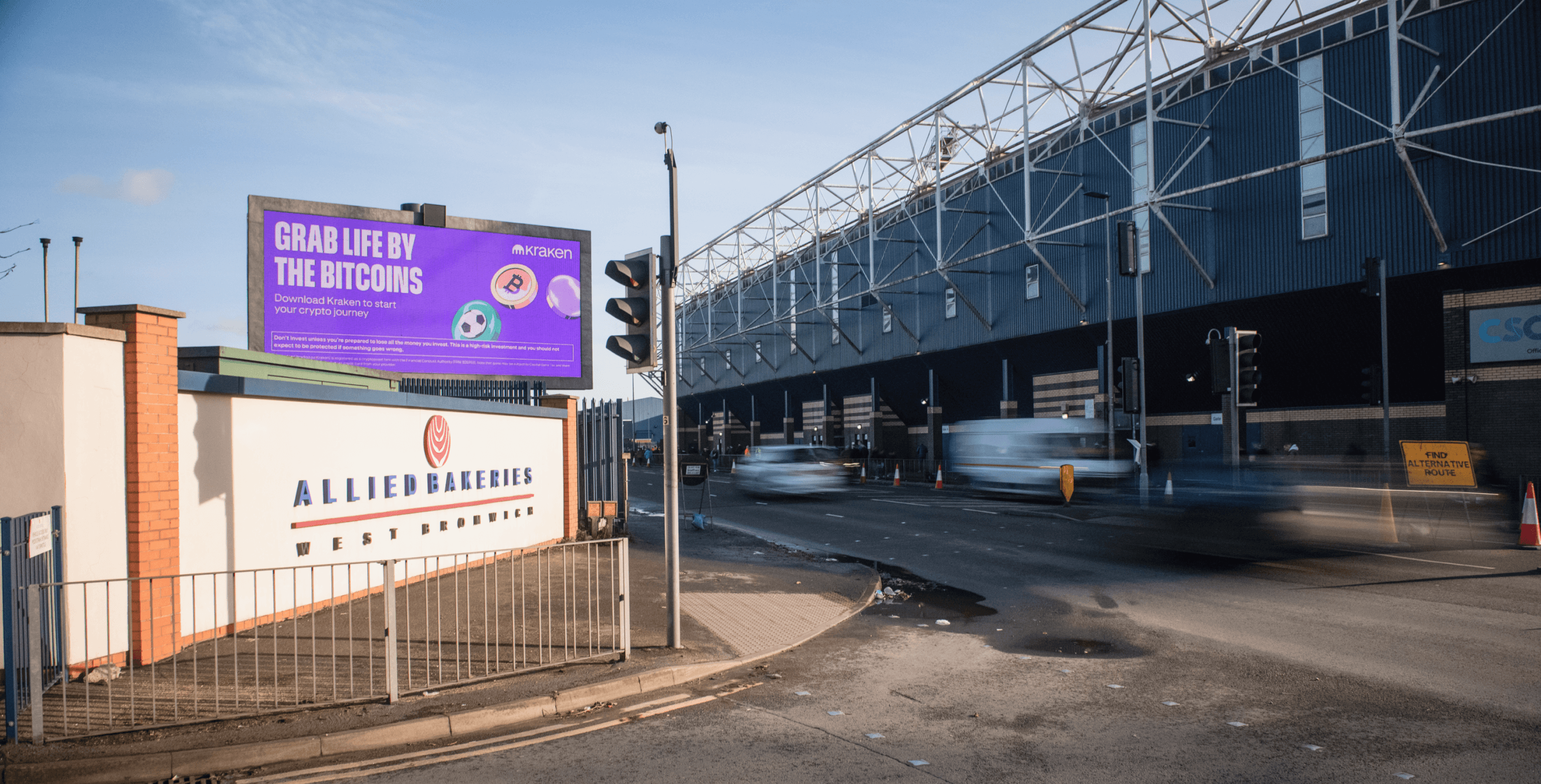 Kraken ‘Grab Life By The Bitcoins’ billboard beside a stadium at dusk