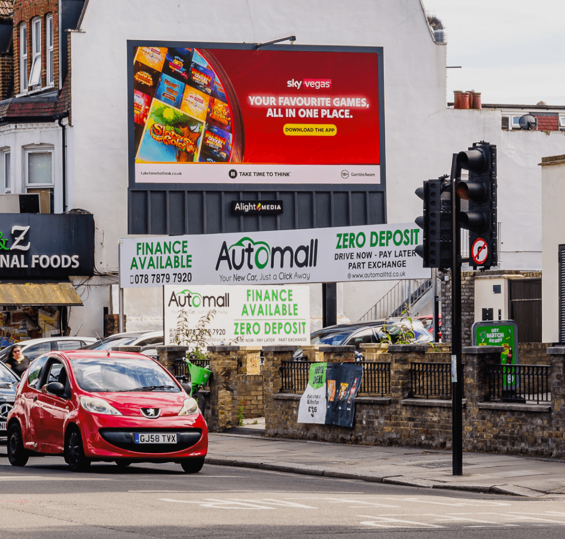 Sky Vegas billboard above an Automall dealership on a daytime high street